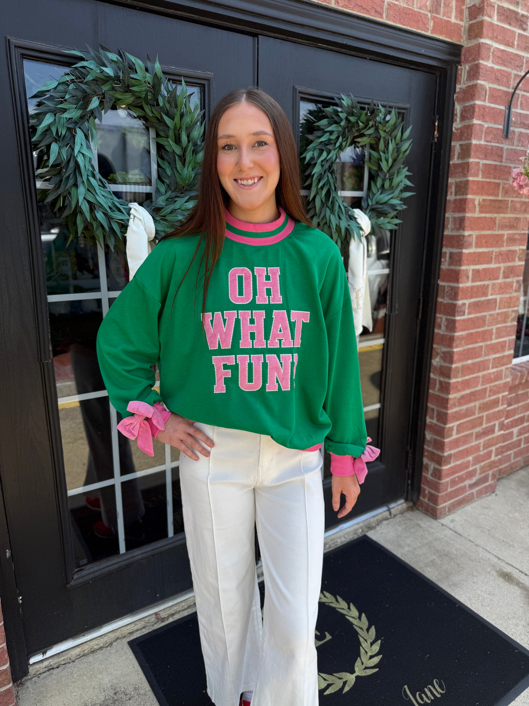 Green Oh What Fun mock neck long-sleeve holiday top with pink trim, cuffs, and “OH WHAT FUN” lettering.