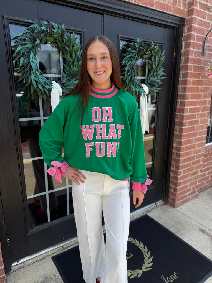 Green Oh What Fun mock neck long-sleeve holiday top with pink trim, cuffs, and “OH WHAT FUN” lettering.