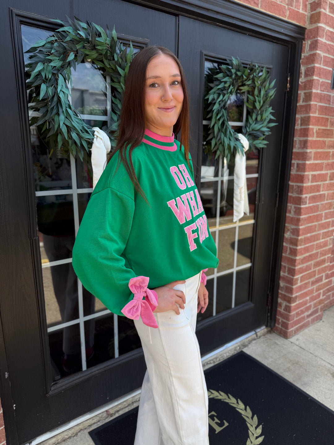 Green Oh What Fun mock neck sweatshirt with pink collar trim, sleeve bows, and “OH WHAT FUN” lettering. Available in all sizes.