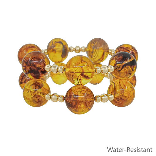 Jet Tortoise Stretch Bracelet Set features two rows of round amber beads with swirling patterns, separated by small gold beads. Stretchy and water-resistant. Sizes available: S, M, L. "Water-Resistant" text in gray at bottom right.