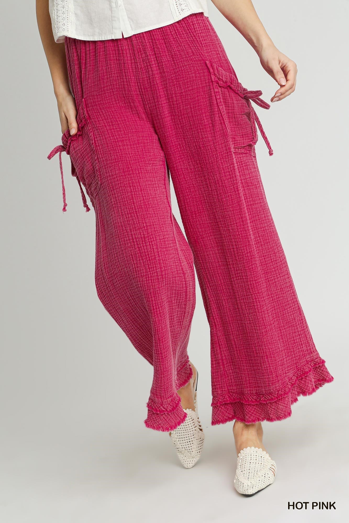 Mineral hot and gauze pants with pockets and on each pocket is a tied bow it is trimmed in rough edged with an extra line of rough trimming. it's color is hot pink mineral washed