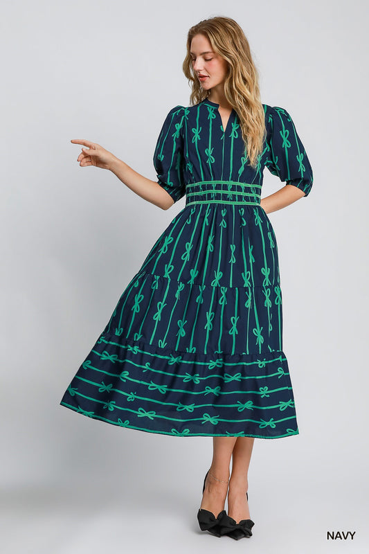 Bow Tie Print Midi Dress: Navy blue fabric with green bow patterns, puff sleeves, velvet trim, fitted waist. Ankle-length. Available in sizes XS to XL.