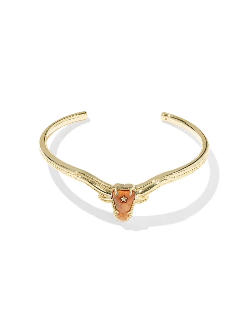Longhorn Gold Cuff Bracelet by Kendra Scott with a shield-shaped orange magnesite centerpiece, star cutout, and ornate gold band detailing; available in one adjustable size.
