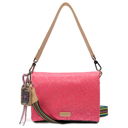 The Metro Crossbody, Bae is a pink glittery bag with a tan shoulder strap, decorative keychain, and detachable striped rainbow strap. Converts into a wristlet. Sizes available: small, medium, large.