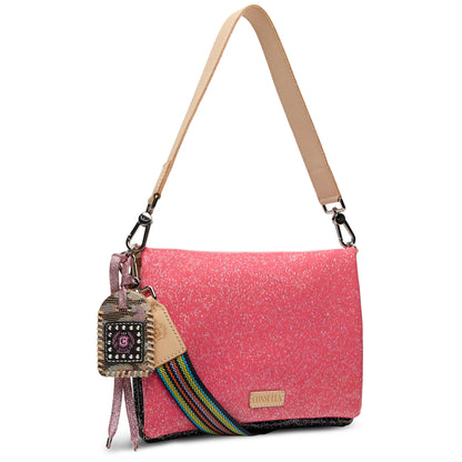 Metro Crossbody, Bae: Pink shoulder bag with beige strap, rainbow accent strap, decorative keychain, and silver clasp. Features a speckled glitter-like texture and small gold front label. Available in small, medium, and large sizes.