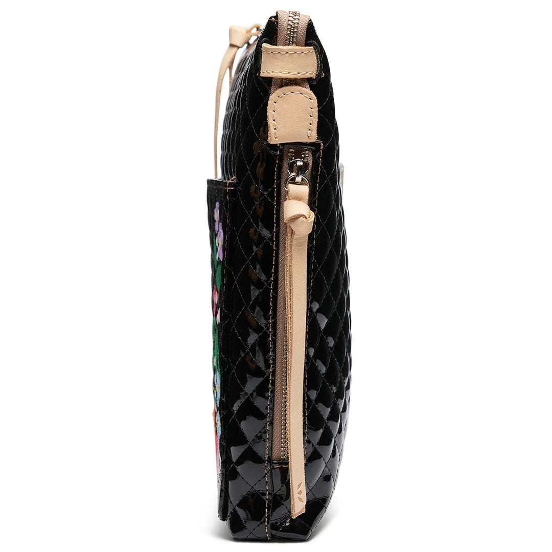 Side view of Tour Crossbody, La Reina—shiny black quilted clutch with tan zipper, leather accents, floral embroidery. Sizes: S, M.