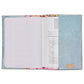 The Consuela Notebook - Lily features a glittery blue ConsuelaCloth™ exterior and a vibrant floral edge on its reusable cover. Inside, lined pages are on the left with printed text on the right. Available in one size.