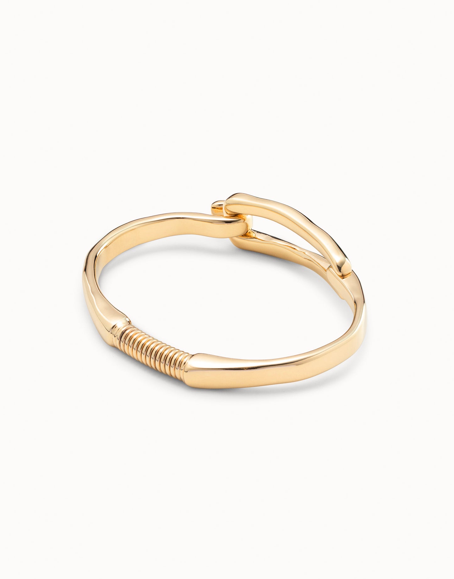 Gold-plated bangle bracelet with buckle-inspired design, handcrafted in Spain by UNOde50, curved band and coiled detail near base. Available sizes: S, M, L.