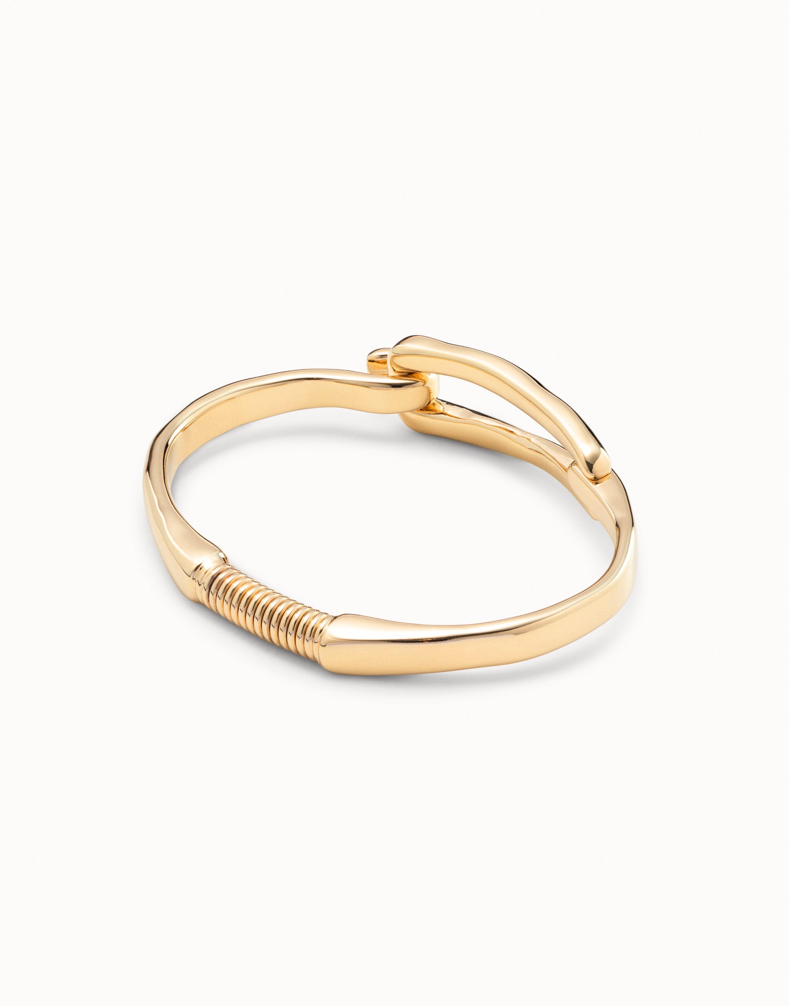 Gold-plated bangle bracelet with buckle-inspired design, handcrafted in Spain by UNOde50, curved band and coiled detail near base. Available sizes: S, M, L.