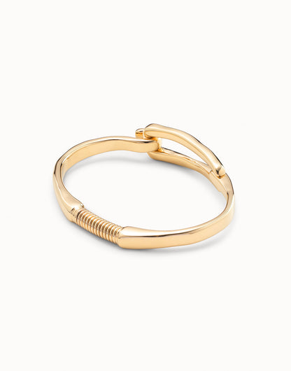 Gold-plated bangle bracelet with buckle-inspired design, handcrafted in Spain by UNOde50, curved band and coiled detail near base. Available sizes: S, M, L.