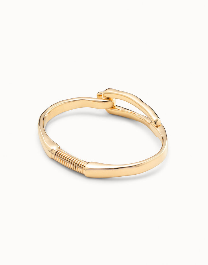 Gold-plated bangle bracelet with buckle-inspired design, handcrafted in Spain by UNOde50, curved band and coiled detail near base. Available sizes: S, M, L.