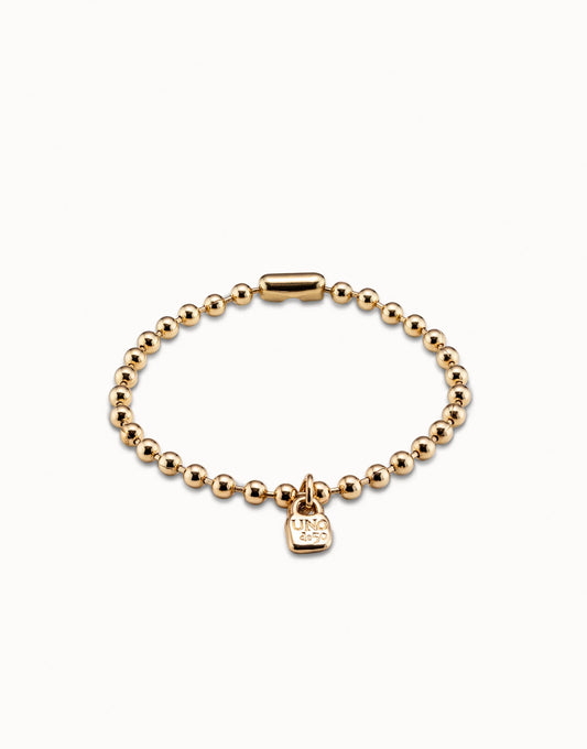 The Beaded Charm Bracelet is handmade in Spain with gold-plated round beads, a cylindrical clasp, and a small rectangular "UNO 50" engraved charm. Available sizes: S, M, L.