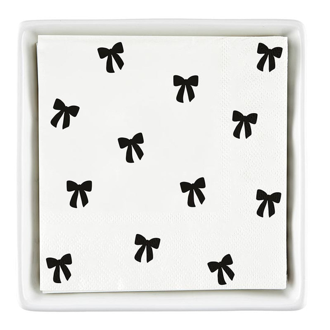 The Ceramic Napkin Tray + Napkins Set includes a ceramic tray with white cocktail napkins featuring black bows. Size: Standard cocktail napkin size.