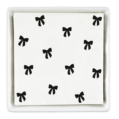 The Ceramic Napkin Tray + Napkins Set includes a ceramic tray with white cocktail napkins featuring black bows. Size: Standard cocktail napkin size.