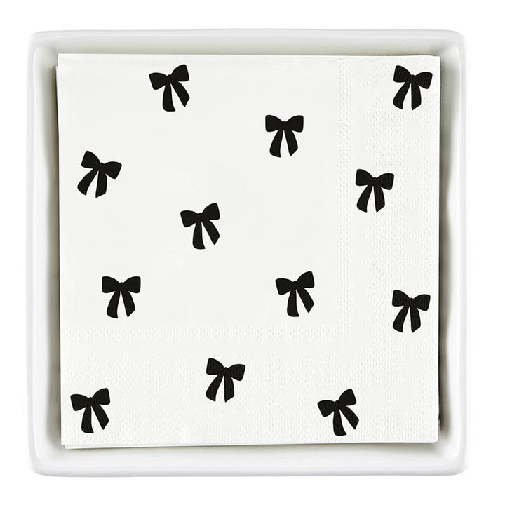 The Ceramic Napkin Tray + Napkins Set includes a ceramic tray with white cocktail napkins featuring black bows. Size: Standard cocktail napkin size.
