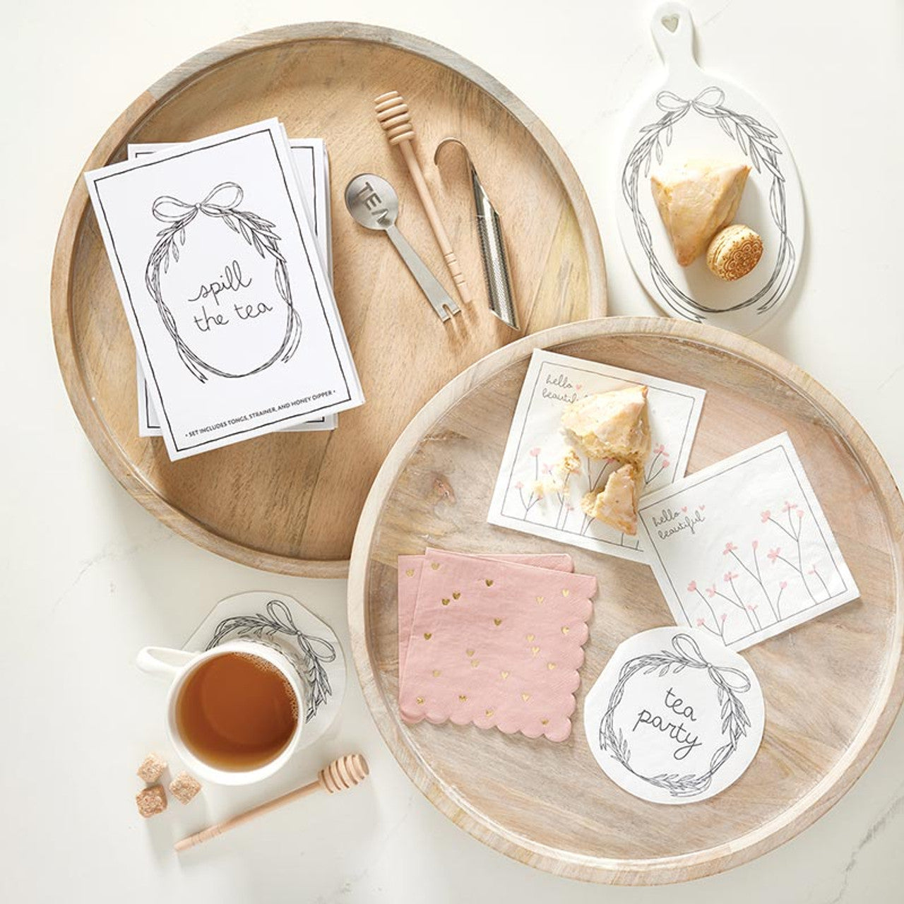 The Tea Essential Book Box - Spill The Tea includes wooden trays, floral design cards, pink napkins, a honey dipper, and a small cup of tea.