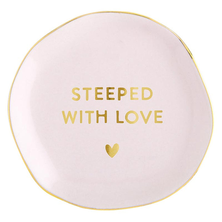 Round, pale pink ceramic tea bag holder with uneven edges and gold trim. Features "STEEPED WITH LOVE" inscription and a small gold heart. Available size: One size.
