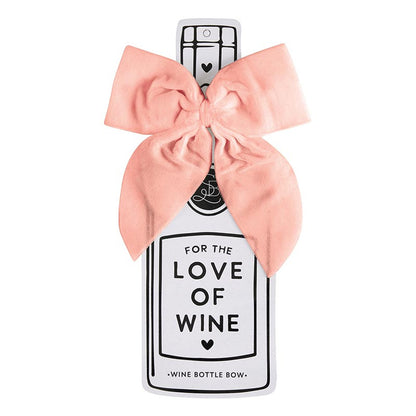 The Velvet Wine Bottle Bow is shaped like a wine bottle and features a large pink velvet bow, decorated with "For the love of wine," "Wine bottle bow," and hearts. Available in one size.