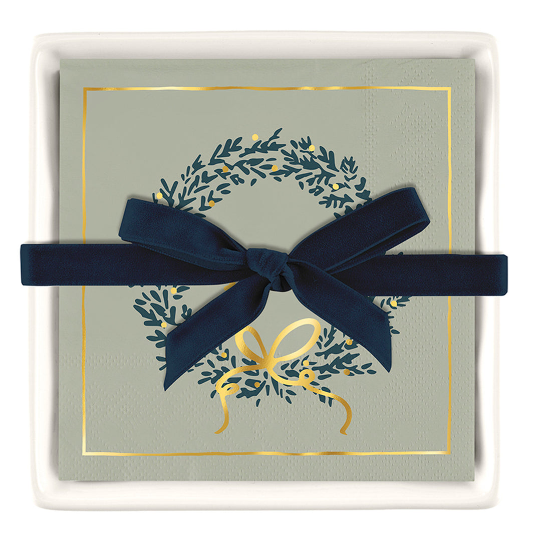 Square white ceramic napkin tray and napkins with a green wreath design, gold border, and navy blue ribbon.