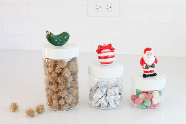 Pinstripes Canister Set: Set of three clear jars with white melamine lids topped by a pickle, striped ball, and Santa ornament. Filled with gold pom-poms, chocolate kisses, and colorful candies. Lids are microwave and dishwasher safe. Sizes: Small (4.25" dia., 6" tall), Medium (4.25" dia., 8.5" tall), Large (4.25" dia., 11" tall).
