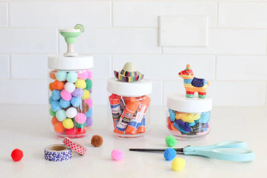 Set of three canisters with melamine lids topped by festive figurines: cocktail glass, sombrero, and piñata. Ideal for storing craft supplies. Sizes available: Small (4" H x 3" Dia), Medium (5" H x 4" Dia), Large (6" H x 5" Dia).