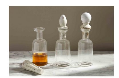Set of three wood finial decanters with white marble stoppers. Available in multiple sizes. One decanter shown with amber liquid.