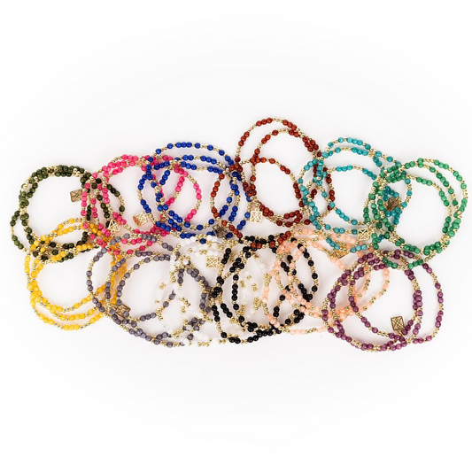 A vibrant array of stretchy bracelets featuring blue, red, green, yellow, pink, purple, and gold with small gold charms. Sizes: S/M and M/L.