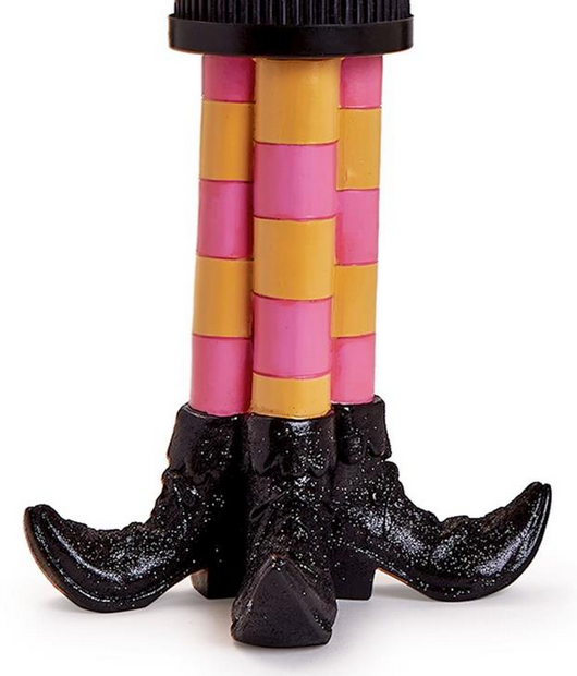 The Bewitching Pillar Candleholder with Glitter Accent features two toy legs in yellow and pink striped stockings and shiny black pointy shoes. Available sizes: small, medium, large.