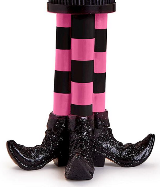 The Bewitching Pillar Candleholder with Glitter Accent features a stand shaped like two legs in pink and black striped stockings with glittery black pointed shoes, resembling a witch’s legs. Available in multiple sizes.