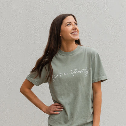 Sage green Eyes on Eternity Tee with "eyes on eternity" in cursive. Available in sizes S-XXL.