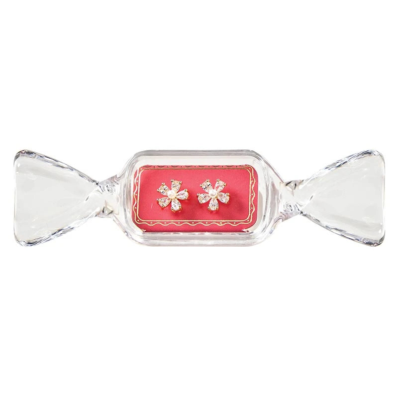 Floral-shaped stud earrings with clear stones and a central pearl in a candy-shaped container.