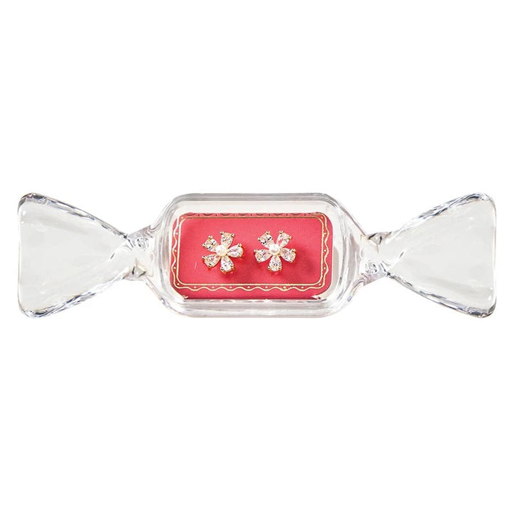 Floral-shaped stud earrings with clear stones and a central pearl in a candy-shaped container.