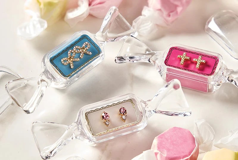 Sweet & Sparkly Candy Dish stud earrings in clear, candy-shaped cases featuring rhinestone bow, cross, and pink gemstone designs.