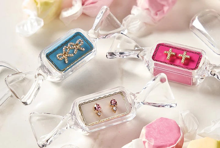 Sweet &amp; Sparkly Candy Dish stud earrings in clear, candy-shaped cases featuring rhinestone bow, cross, and pink gemstone designs.