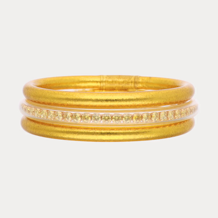 Gold ring with matte finish, three parallel bands, center band set with small clear gemstones. Available in sizes 5-9.