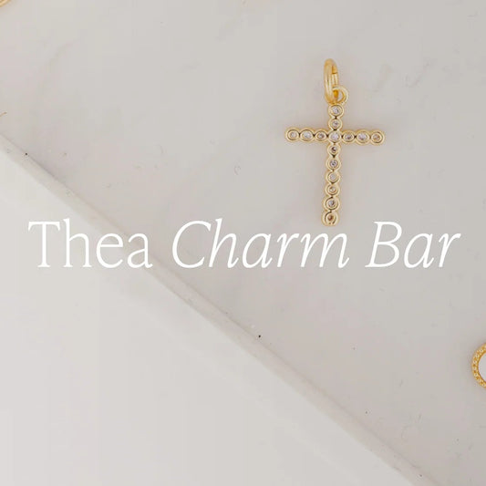 A delicate 18k gold-plated cross pendant with small circular accents, available in multiple sizes. Customizable as part of the Thea Charm Bar collection.