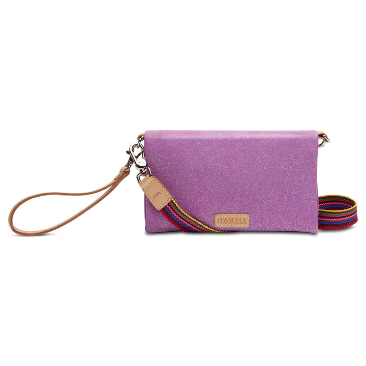 Small glittery purple rectangular clutch with tan leather wristlet, detachable rainbow-striped shoulder strap, zipper compartments, and front tan leather "CONSUELO" patch. Available in one size.