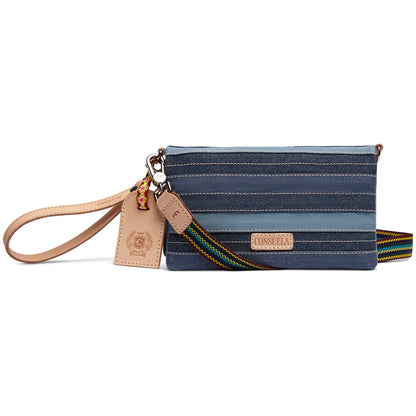 The Uptown Crossbody, Royal is a small blue striped pouch with a tan leather strap, colorful woven wristlet accent, and Consuela logo leather tag. Features fabric exterior, zipper closure, and card holder slots inside. Size availability not specified.