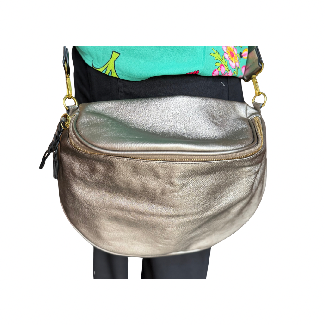 The Megan Sling Bag is a metallic gold, curved, vegan leather crossbody with zipper closure. Available in S, M, and L.