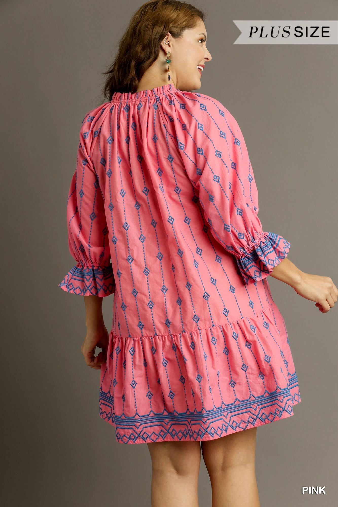 The Embroidery Short A-Line Dress with Split Ruffle Neckline & Tassel Tie is a plus-sized pink frock adorned with blue embroidery. This dress features long sleeves and a tiered skirt for added flair. Available in multiple plus sizes.