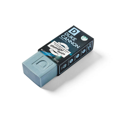 Blue rectangular Duke Cannon "Big Ass Brick of Soap - Midnight Swim," 10 oz., shown partly out of its black box with product info.