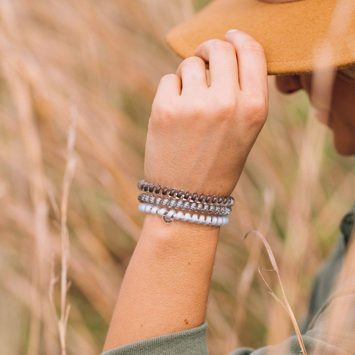 Three coiled TELETIES Hair Ties in gray, brown, and white; available in small and large sizes.