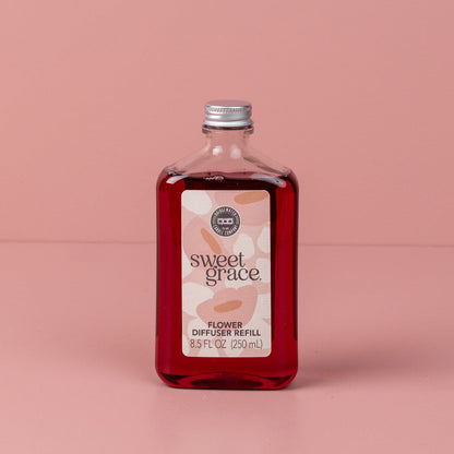 Clear bottle labeled "Sweet Grace Flower Diffuser Refill," red liquid, oriental spice scent; available in 8 oz or 17 oz sizes.