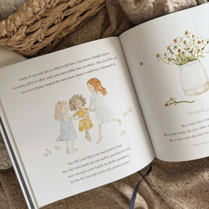 Open Bedtime Blessings book with watercolor illustrations of three children holding hands and a jar of wildflowers, including a printed bedtime blessing.