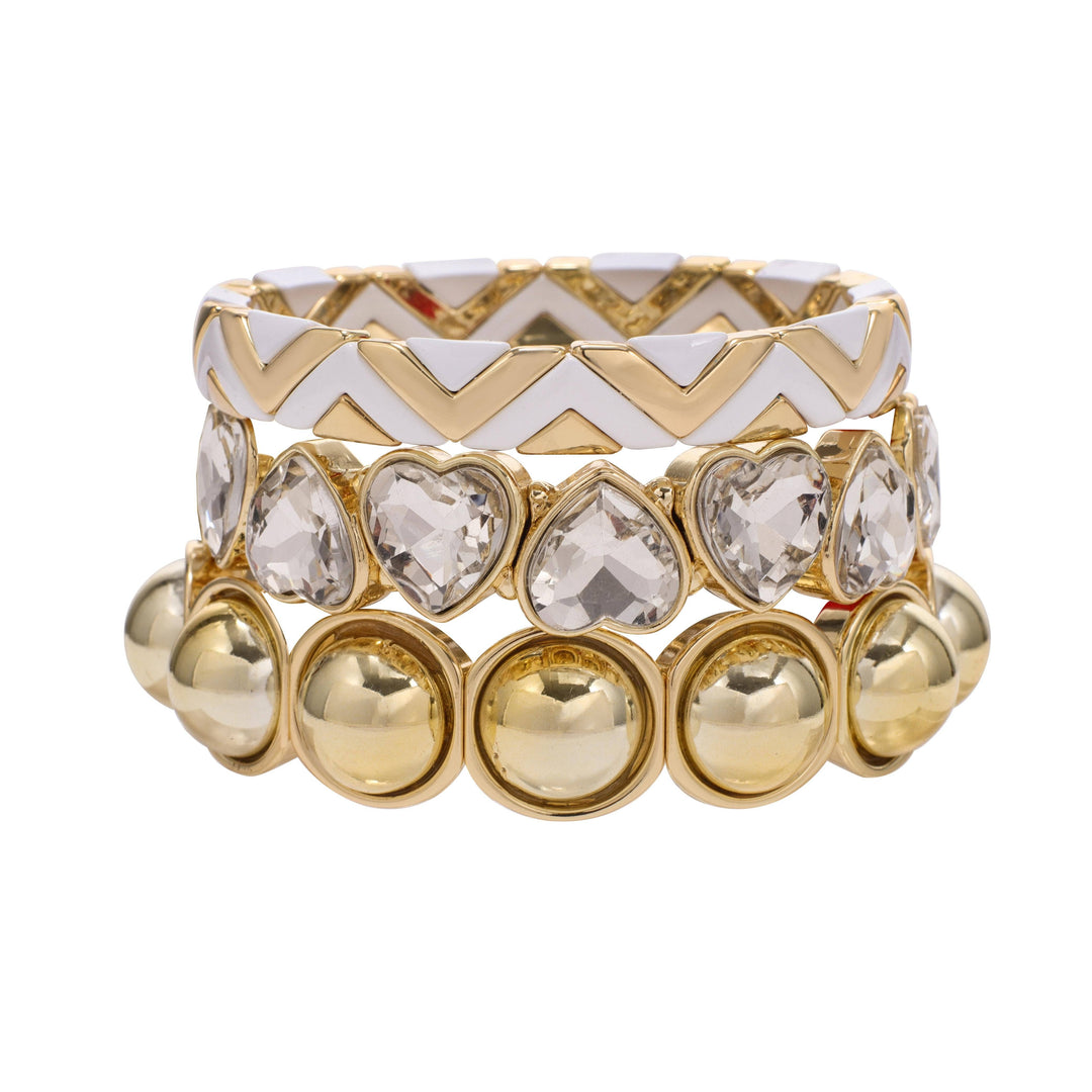 Three gold stretch bracelets: white chevron enamel, heart-shaped crystals, round gold domes. Available in S/M, M/L.