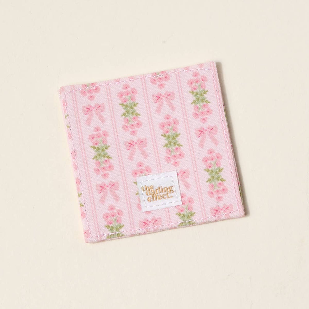 Pink fabric bookmark with floral and bow print, vertical stripes, gold "the darling effect" label; sizes available.