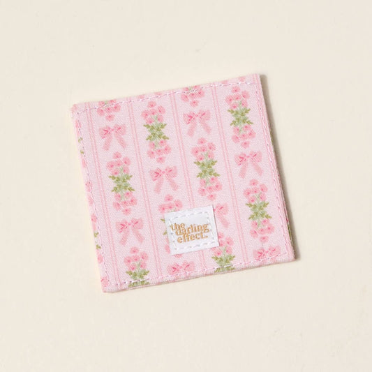 Pink fabric bookmark with floral and bow print, vertical stripes, gold "the darling effect" label; sizes available.