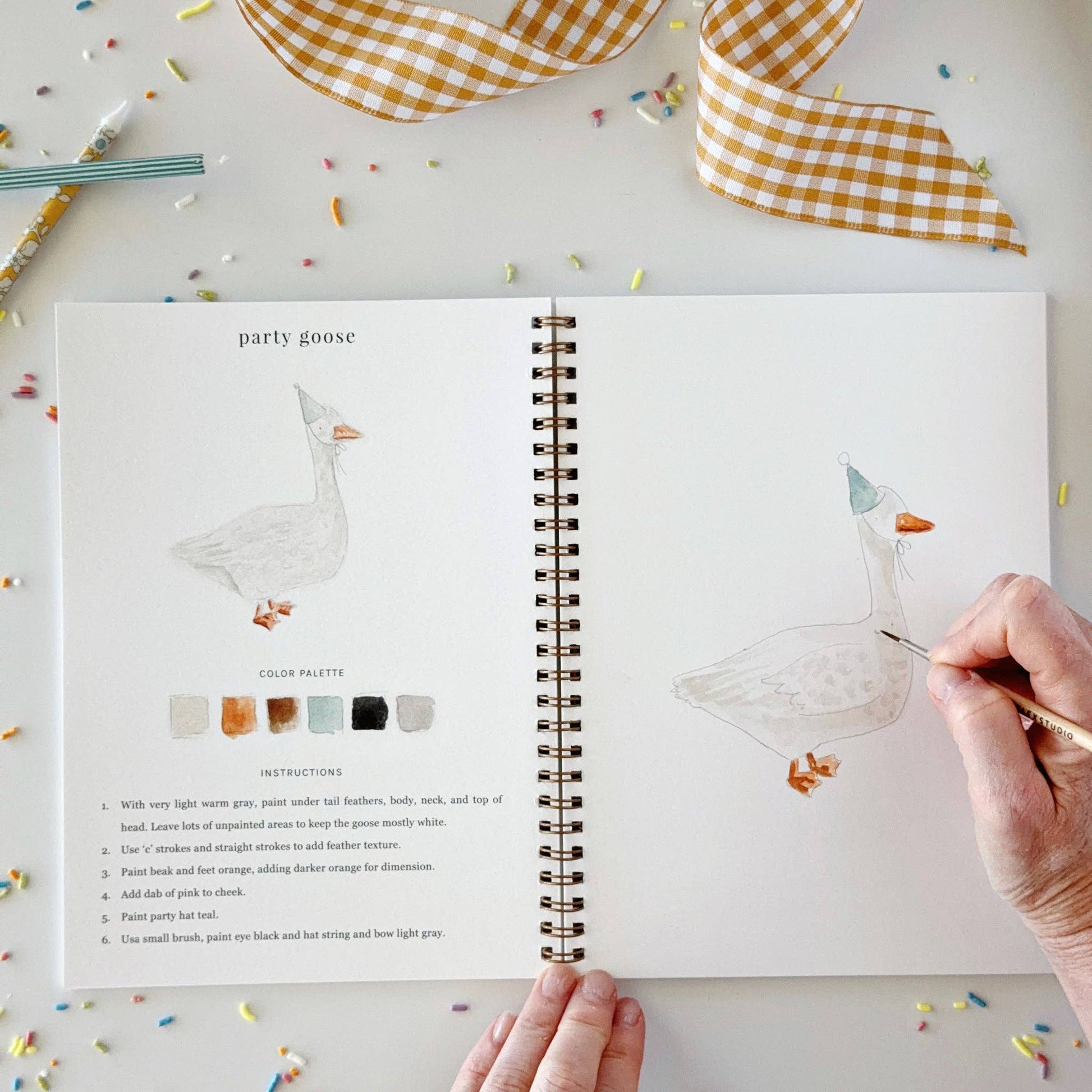 Celebrate watercolor workbook, open to a “party goose” page with step-by-step painting instructions and a hand-drawn goose in a party hat. Available in multiple sizes.
