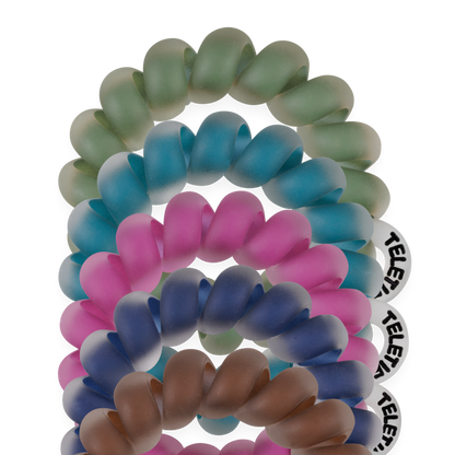 Set of five coiled, frosted Tiny Hair Ties in green, blue, purple, pink, and brown, each with a round white tag. Available in kids and fine hair sizes.