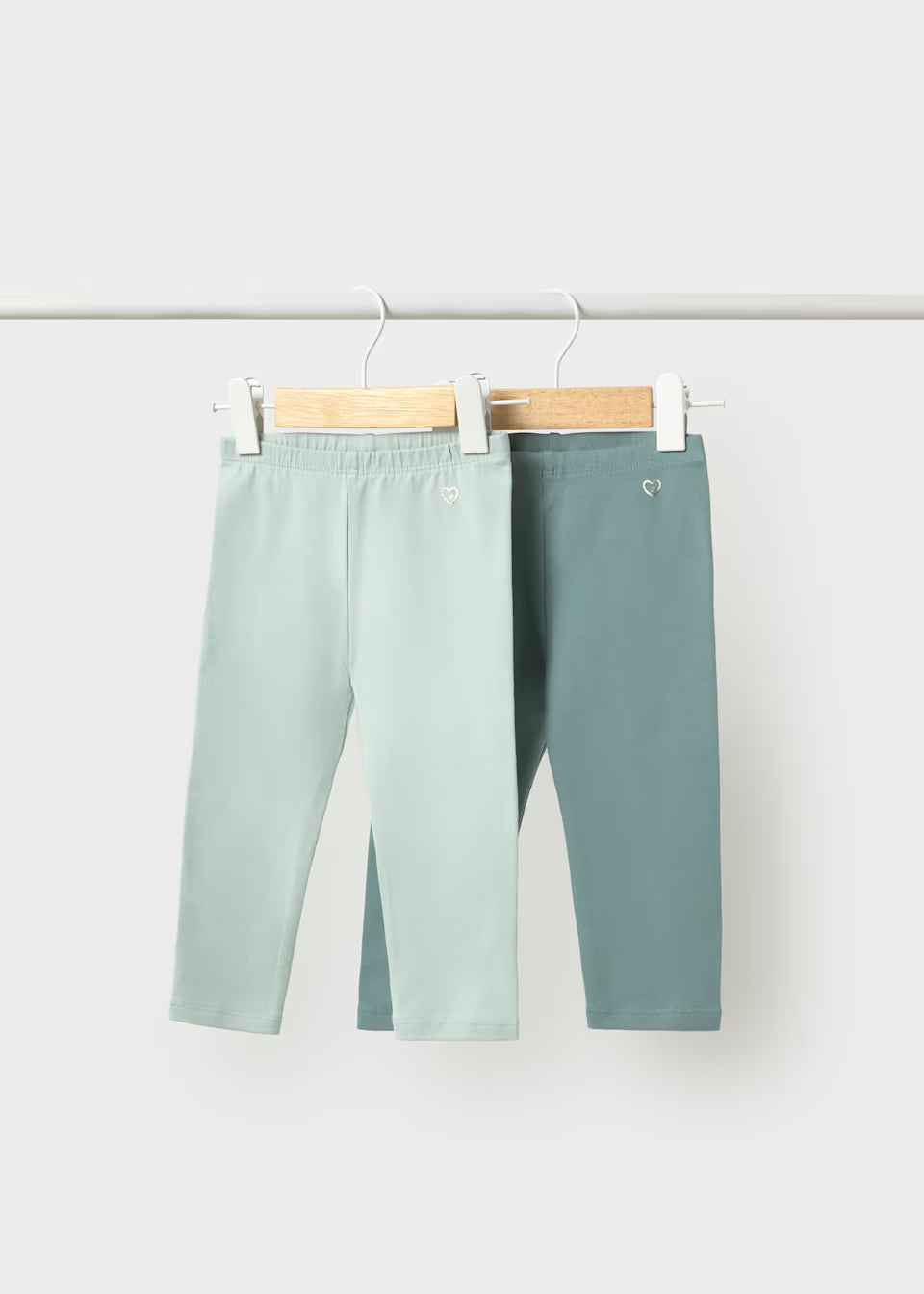 The Little Girl 2-Pack Basic Leggings Set includes one light green and one teal cotton legging, each with a small heart near the waist. Available in sizes 2T-6X.